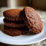 A stack of four dark brown, textured soft gingerbread cookies resting on a white plate.