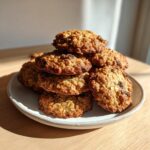 A tempting stack of freshly baked, soft oatmeal raisin cookies piled high on a light-colored plate.