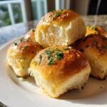 A stack of fluffy, golden sourdough discard rolls brushed with melted butter and topped with fresh parsley.