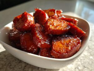 Close-up of thick-cut, glossy southern candied yams swimming in a rich, dark glaze inside a white bowl.