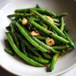 Close-up of bright green, cooked dilly beans seasoned with chili flakes and whole garlic cloves.