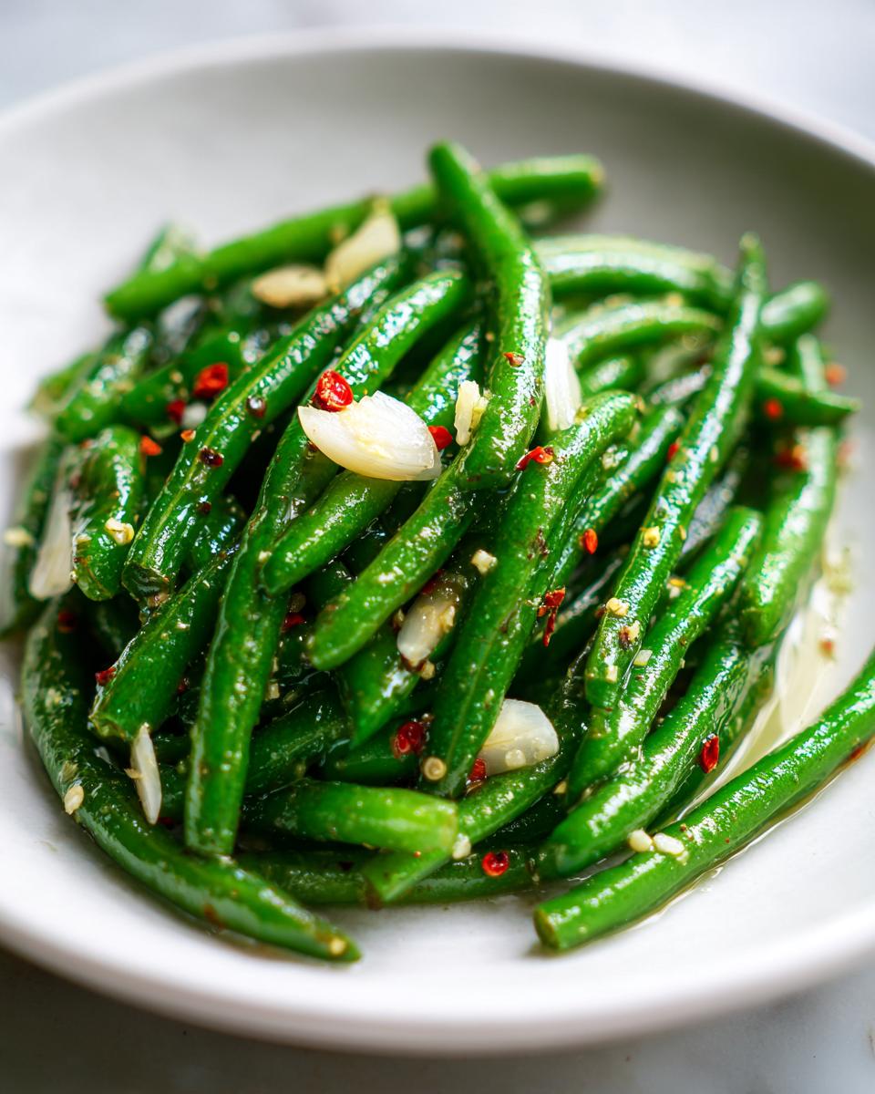 Close-up of vibrant green dilly beans tossed with sliced garlic and red pepper flakes.