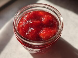 Overhead close-up of bright red strawberry freezer jam with whole fruit pieces in a glass jar.