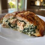 A cross-section view of a perfectly cooked stuffed salmon fillet showing creamy spinach filling inside.