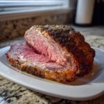 A thick slice of perfectly cooked rib roast showing a pink, medium-rare center and a seasoned, browned crust.