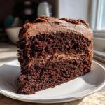 Close-up of a rich, moist slice from the ultimate 1-bowl chocolate cake recipe, topped with thick chocolate frosting.