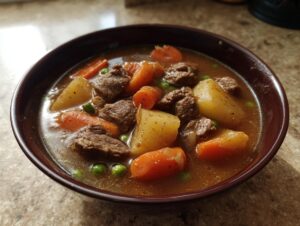 Close-up of a rich bowl of vegetable beef soup featuring tender beef chunks, large potato pieces, carrots, and peas.