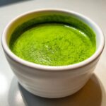 Close-up of a small white bowl filled with bright green, creamy spinach soup.