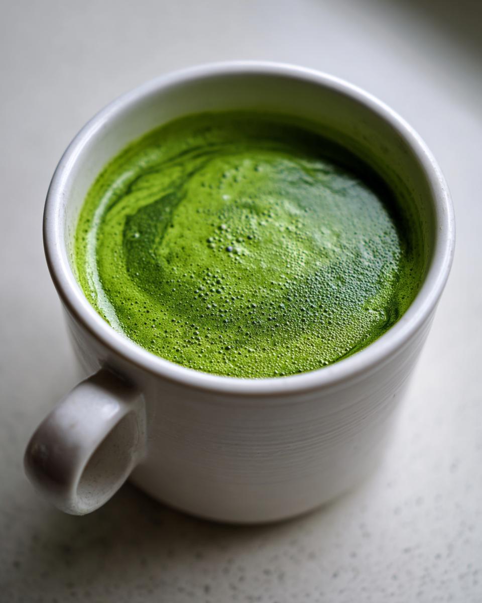 Close-up of a vibrant green liquid, resembling a creamy spinach soup, served in a white mug.