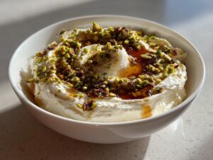 A white bowl filled with creamy whipped ricotta dip, drizzled with honey and topped with chopped pistachios.