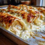 Close-up of baked white chicken enchiladas overflowing with shredded chicken and melted, bubbly cheese.
