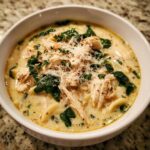 A close-up of a bowl of rich white chicken lasagna soup, featuring shredded chicken, spinach, and grated Parmesan cheese.