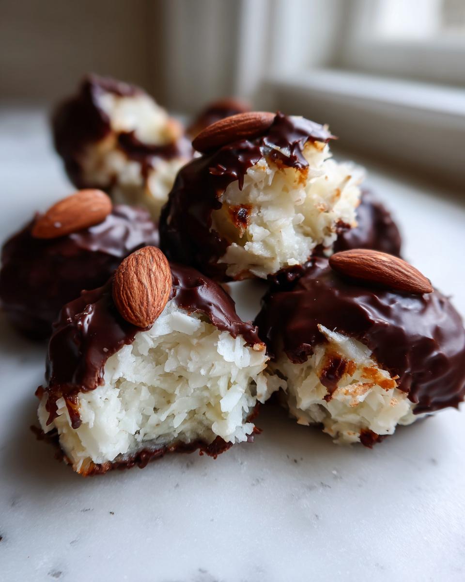 Close-up of several homemade almond joy truffles, showing the white coconut filling dipped in dark chocolate and topped with a whole almond.