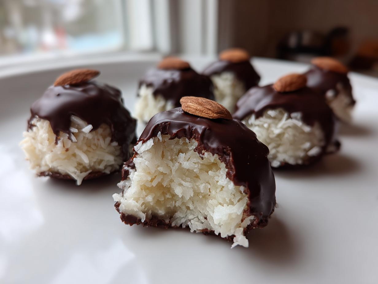 Close-up of homemade almond joy truffles showing the shredded coconut interior, dipped in dark chocolate, and topped with an almond.