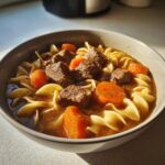 Close-up of a bowl of amazing 1-pot beef noodle soup with chunks of beef, carrots, and egg noodles.