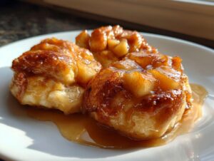 Three golden brown, glazed apple dumpling pastries covered in sweet cinnamon caramel sauce on a white plate.