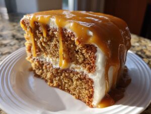 Close-up of a moist slice of caramel cake layered with white frosting and generously topped with dripping caramel sauce.