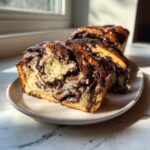 A close-up of a sliced chocolate babka showing the rich swirl pattern and glossy chocolate glaze.