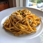 Close-up of a serving of creamy crab pasta, topped with generous flakes of white crab meat and chopped parsley.