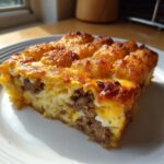 A thick slice of savory egg bake with ground meat, cheese, and a golden tater tot crust.