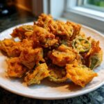 A generous pile of perfectly golden brown fried okra pieces served on a white plate.