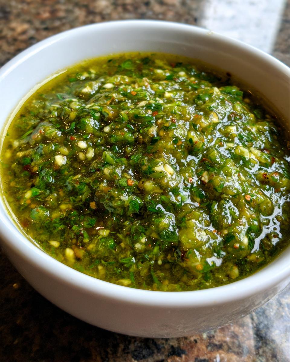 Close-up of chunky, bright green tomato salsa with visible seeds and herbs in a white serving bowl.