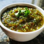 A close-up, vibrant image of amazing green tomato salsa, chunky and green, topped with fresh cilantro in a white bowl.