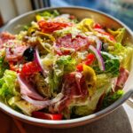 A vibrant bowl of grinder salad featuring lettuce, salami, ham, red onion, peppers, and creamy dressing.