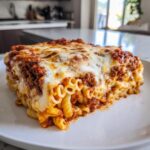A generous square slice of baked pasta bake layered with meat sauce and melted mozzarella cheese on a white plate.