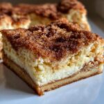 A close-up, tempting slice of amazing sopapilla cheesecake showing layers of crust, cream cheese filling, and cinnamon sugar topping.