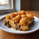 A hearty serving of tater tot casserole featuring crispy tots, melted cheese, and ground beef mixture on a white plate.