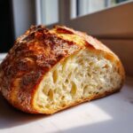 Close-up of a freshly baked artisan bread loaf, showing a deeply caramelized crust and an open, airy crumb structure.