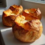 Four freshly baked, golden-brown bread bowls sitting on a counter in bright sunlight.