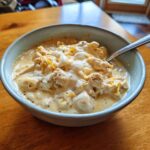 A close-up of a bowl of creamy, cheesy cream cheese chicken chili topped with melted cream cheese and shredded cheddar.