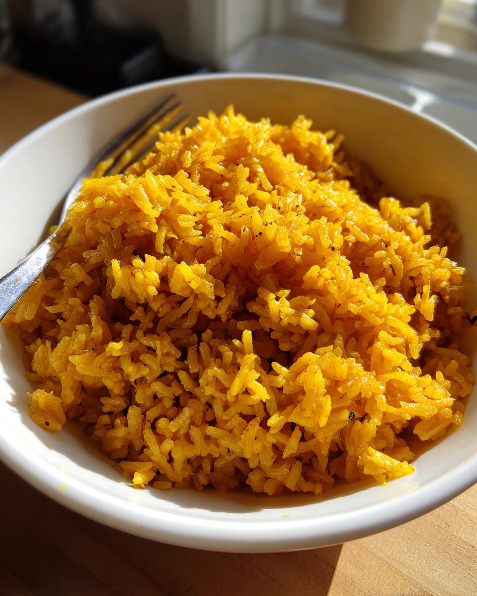A close-up of fluffy, bright yellow turmeric rice served in a white bowl with a fork resting on the side.