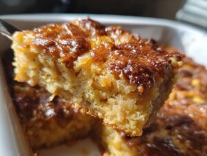 A close-up shot showing a fork lifting a moist, golden piece of caramel apple dump cake with a shiny, caramelized top.