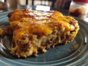 A close-up shot of a hearty slice of john wayne casserole topped with melted, browned cheddar cheese.