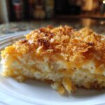 Close-up of a slice of cheesy potato casserole with a golden, crunchy cornflake topping.
