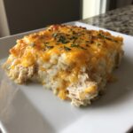 A square serving of chicken cauliflower rice casserole topped with melted cheddar cheese and parsley.