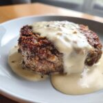 Close-up of a golden brown chicken fried steak smothered in creamy white pepper gravy.