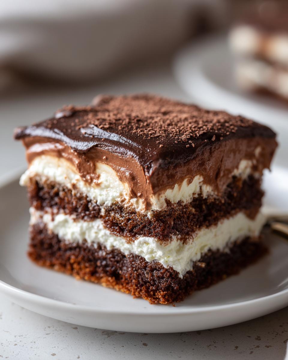 A rich, layered slice of chocolate Italian love cake featuring dark cake, white cream, and chocolate frosting dusted with cocoa.