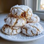 A stack of five christmas gooey butter cookies heavily dusted with powdered sugar on a white plate.