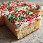 Close-up of a thick slice of Christmas sugar cookie bars topped with white frosting and red and green sprinkles.