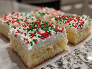 Four squares of fluffy Christmas sugar cookie bars topped with white frosting and red, green, and white sprinkles.