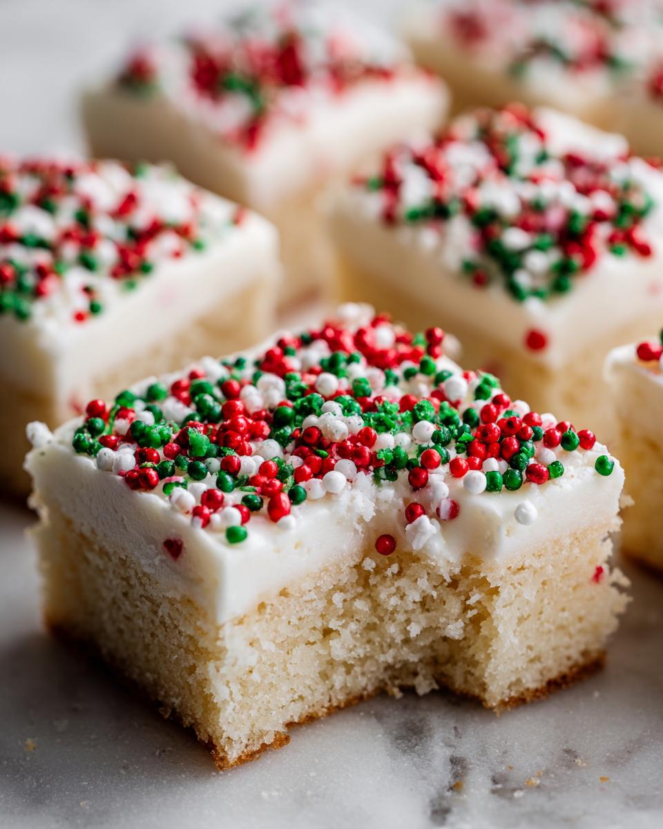 A close-up of a square Christmas sugar cookie bars piece with white frosting and red, green, and white sprinkles, showing a bite taken out.