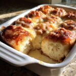 Close-up of freshly baked cinnamon rolls with heavy cream soaking the bottom, served in a white baking dish.