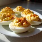 Six halves of creamy deviled eggs, generously filled and sprinkled with paprika, served on a white plate.