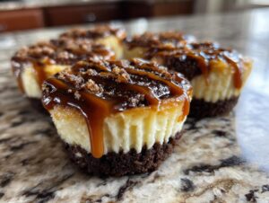 Close-up of several rich cookie butter cheesecake cups topped with caramel sauce and cookie crumbs.