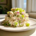 A mound of creamy cottage cheese chicken salad mixed with bright green celery and red onion pieces on a white plate.