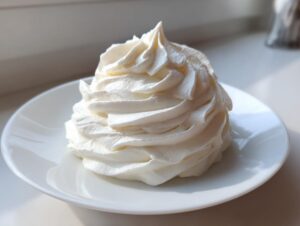 A beautiful, tall swirl of fluffy white cream cheese frosting piped onto a small white plate.